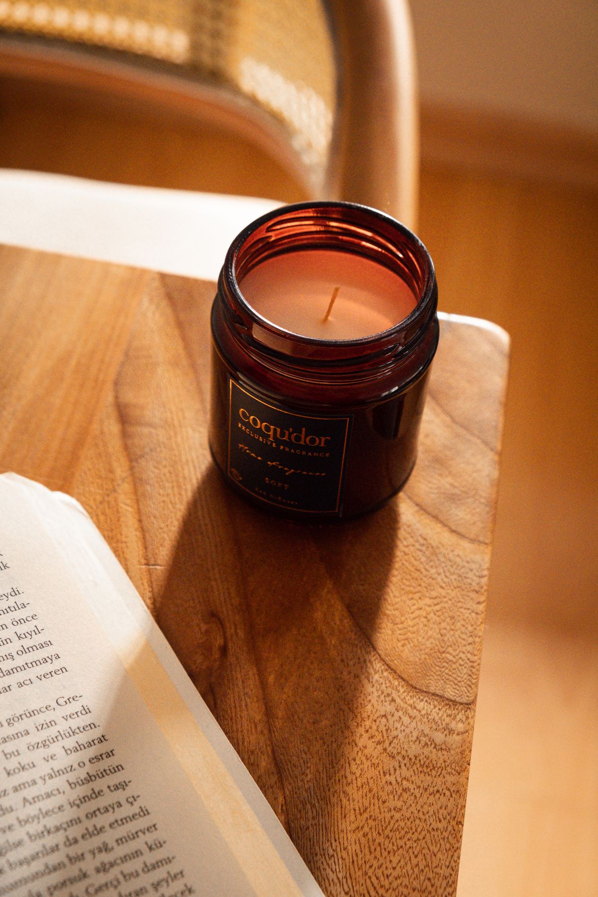 An amber glass candle beside an open book on a wooden table.